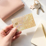 Hand holding a gold glitter debit card skin with keys on a soft pink background by The Sticker Era