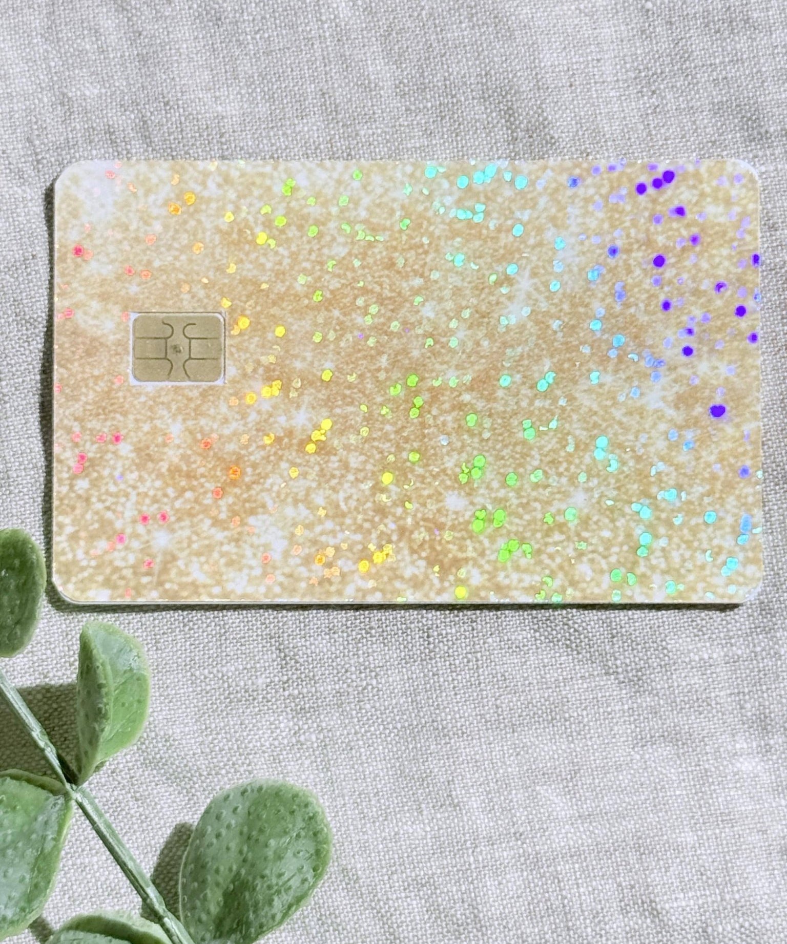 Sparkly gold glitter card skin laid flat with eucalyptus and confetti by The Sticker Era