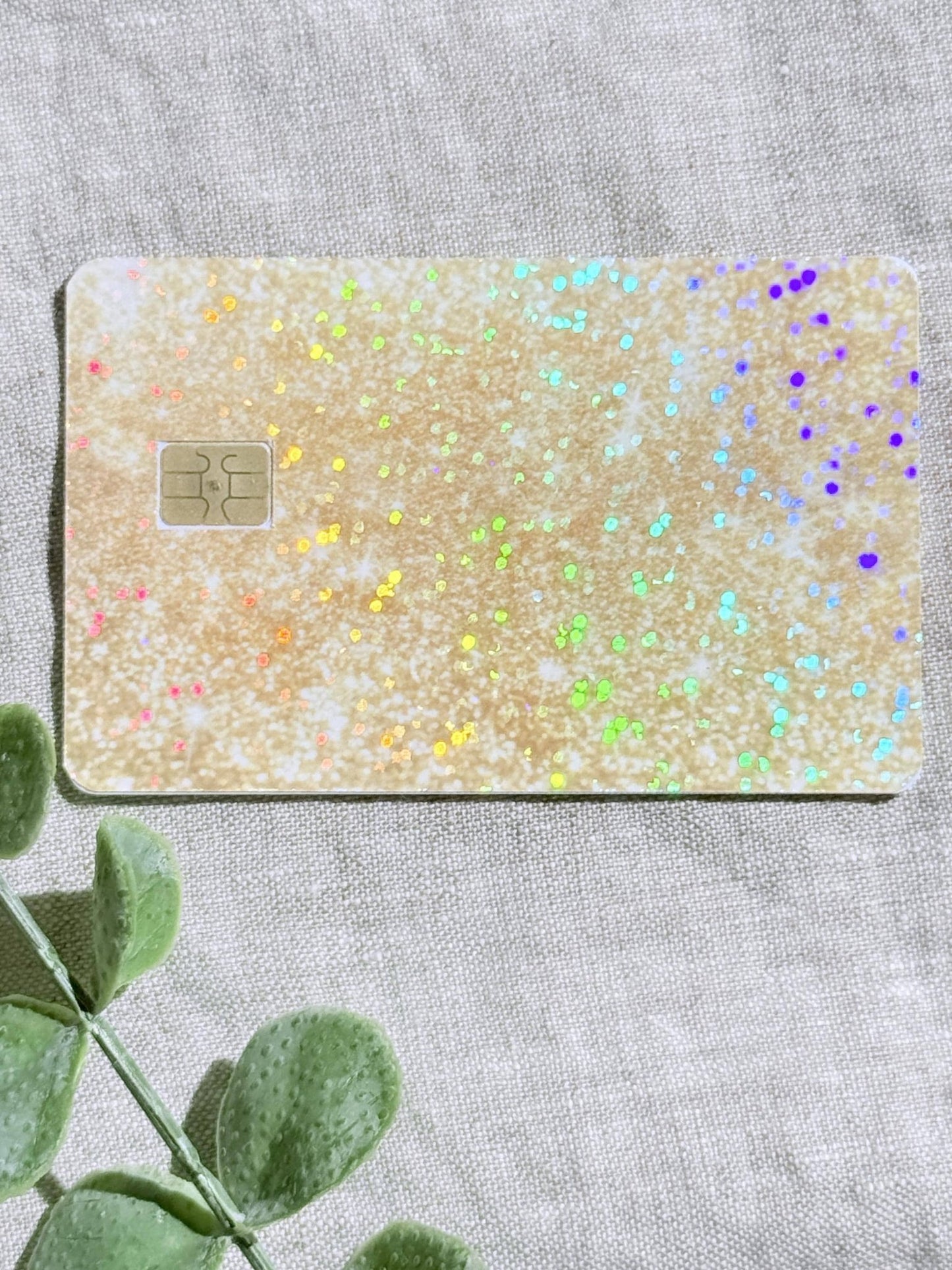 Sparkly gold glitter card skin laid flat with eucalyptus and confetti by The Sticker Era