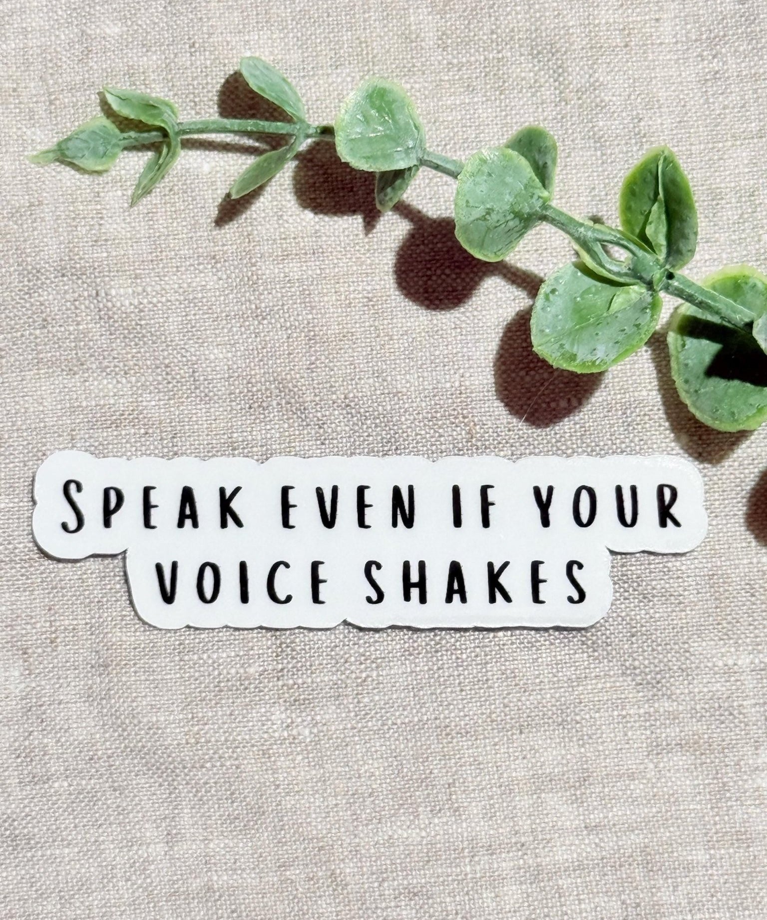 Speak Even If Your Voice Shakes" empowerment sticker on linen with eucalyptus