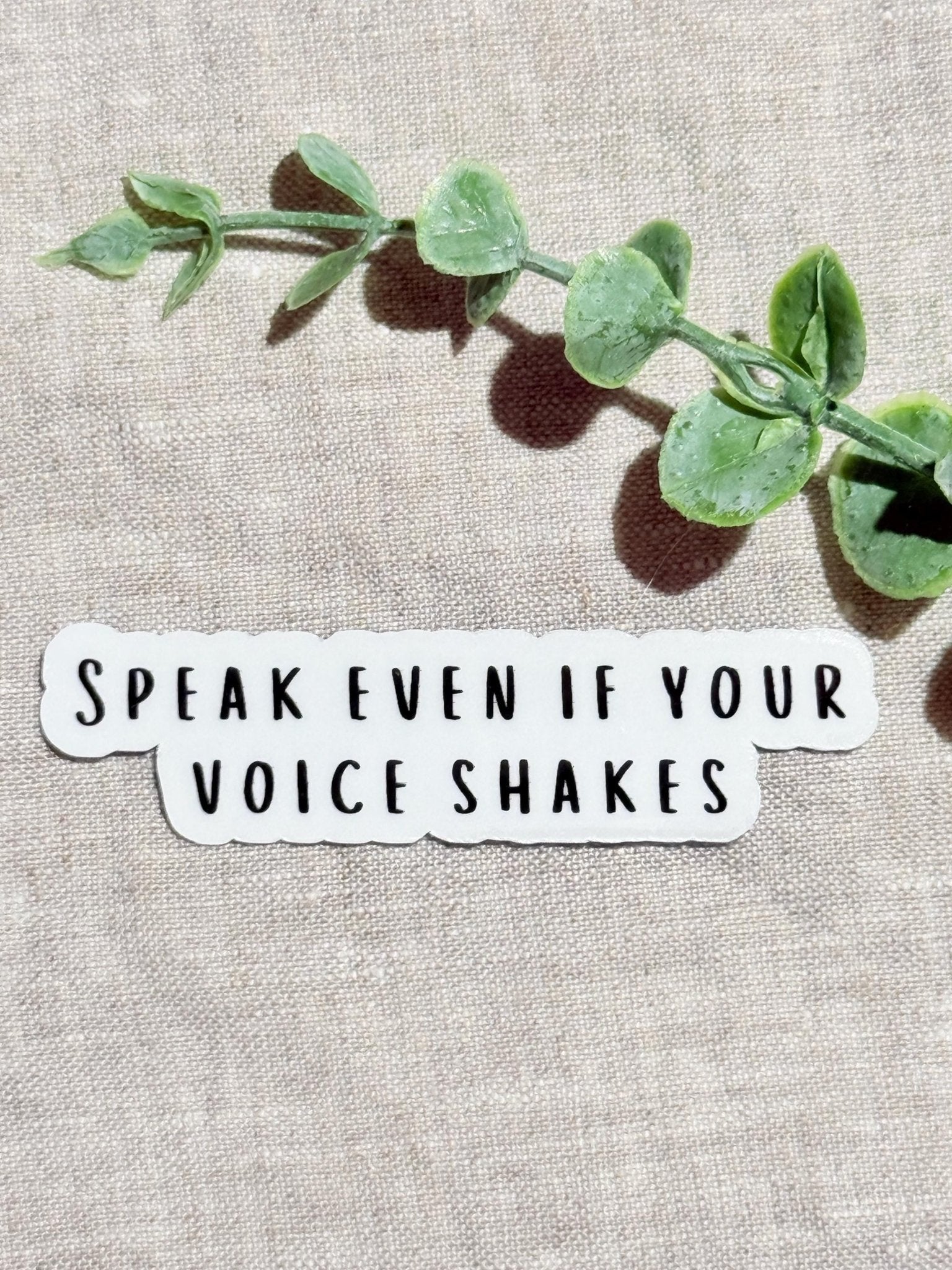 Speak Even If Your Voice Shakes" empowerment sticker on linen with eucalyptus