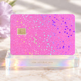 Holographic pink glitter debit card skin on an acrylic stand in soft sunlight by The Sticker Era