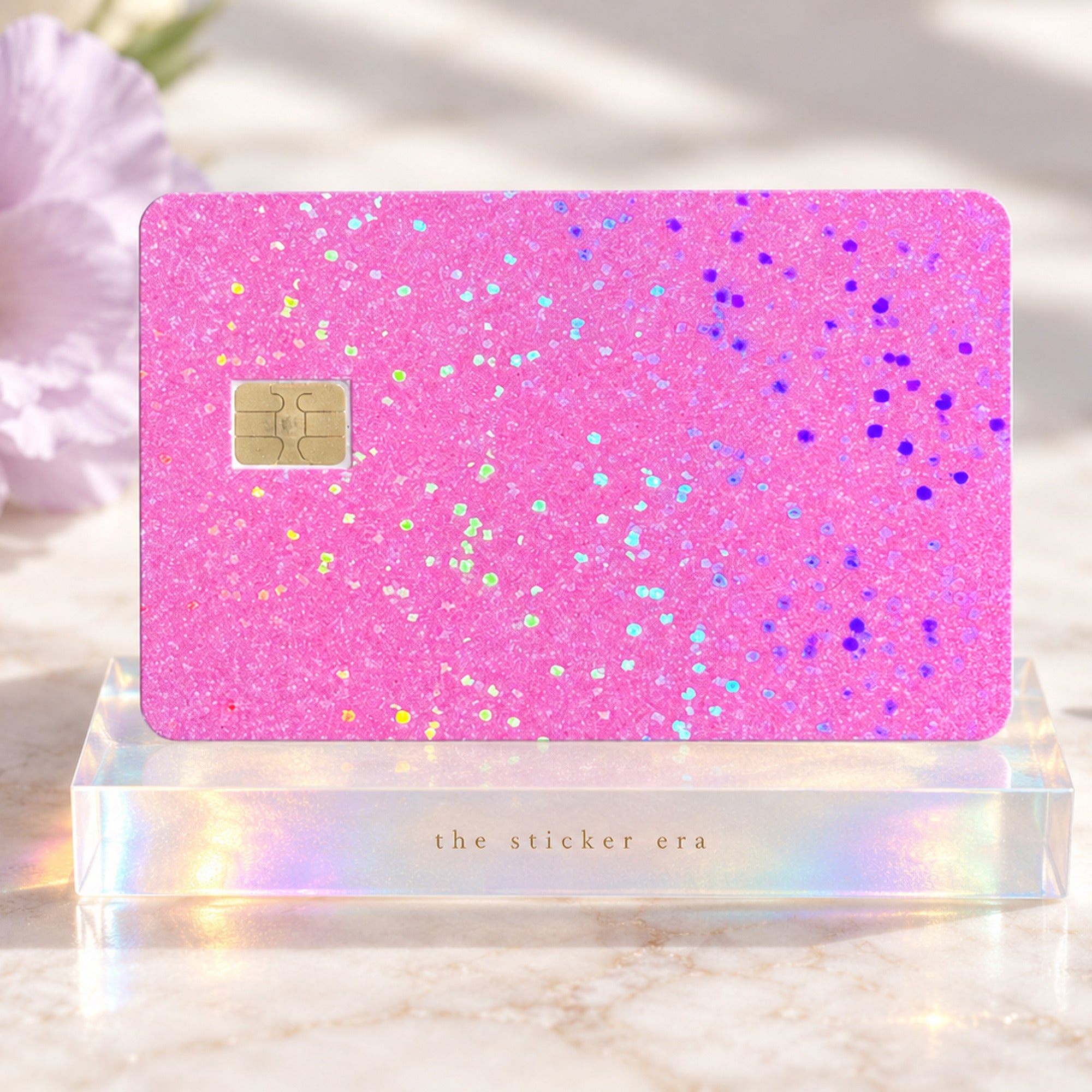Holographic pink glitter debit card skin on an acrylic stand in soft sunlight by The Sticker Era