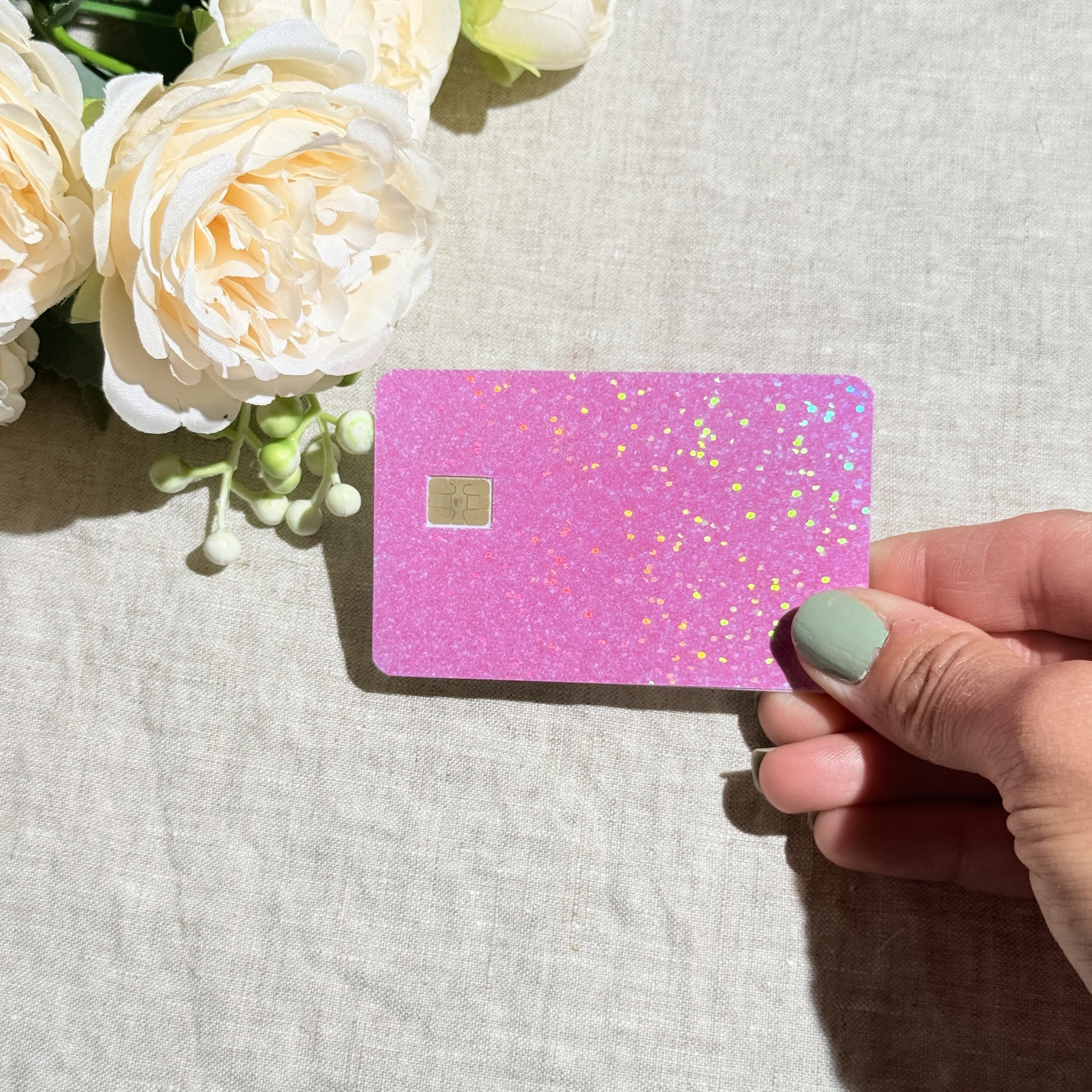 Hand holding the light pink holographic glitter card skin in sunlight by The Sticker Era