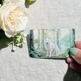 Hand holding the white wolf forest debit card skin in sunlight by The Sticker Era