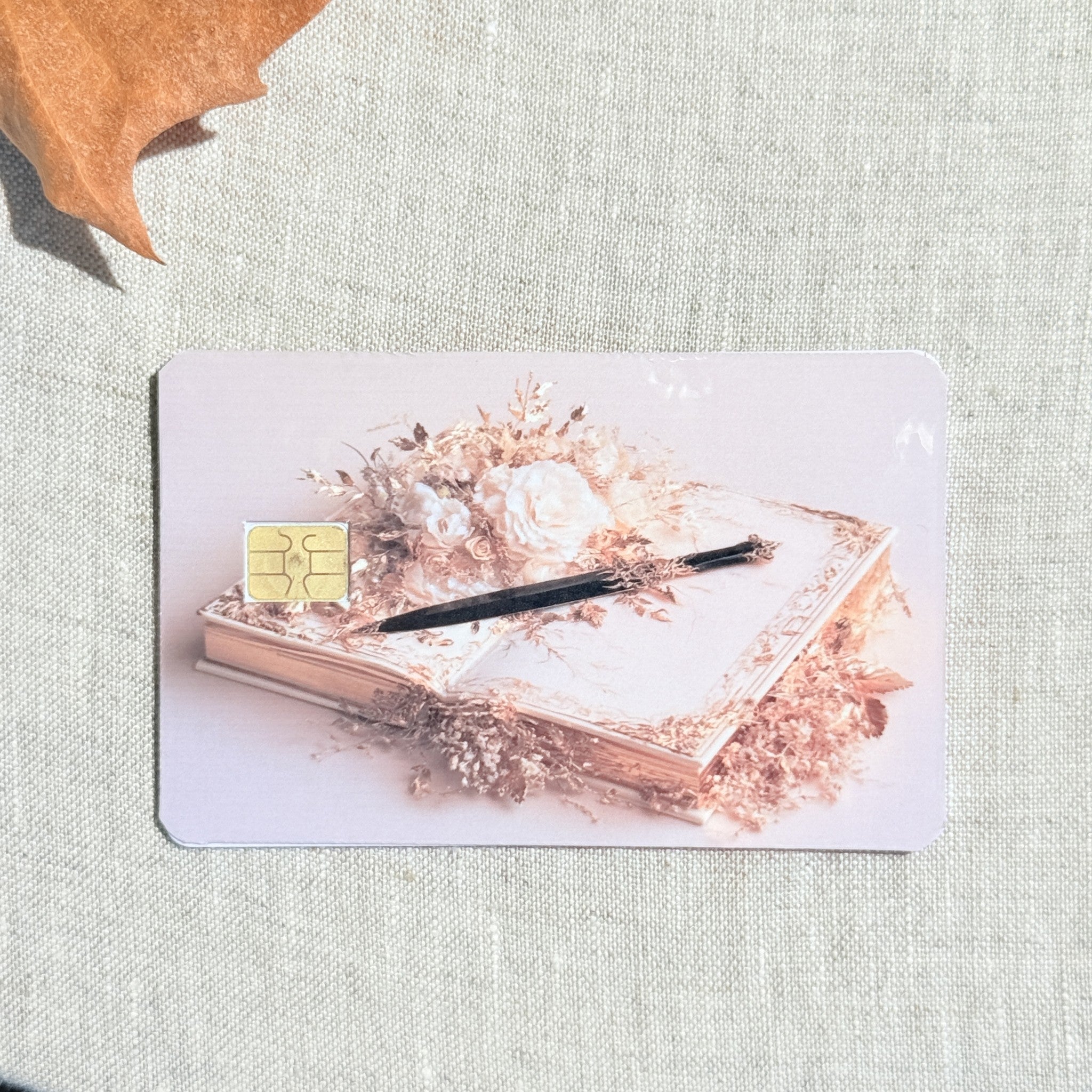 Quill and roses card skin on a debit card, dark pen on an open book with blush roses