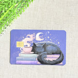 Sleepy cat card skin on a debit card, grey cat asleep on pastel books under a crescent moon