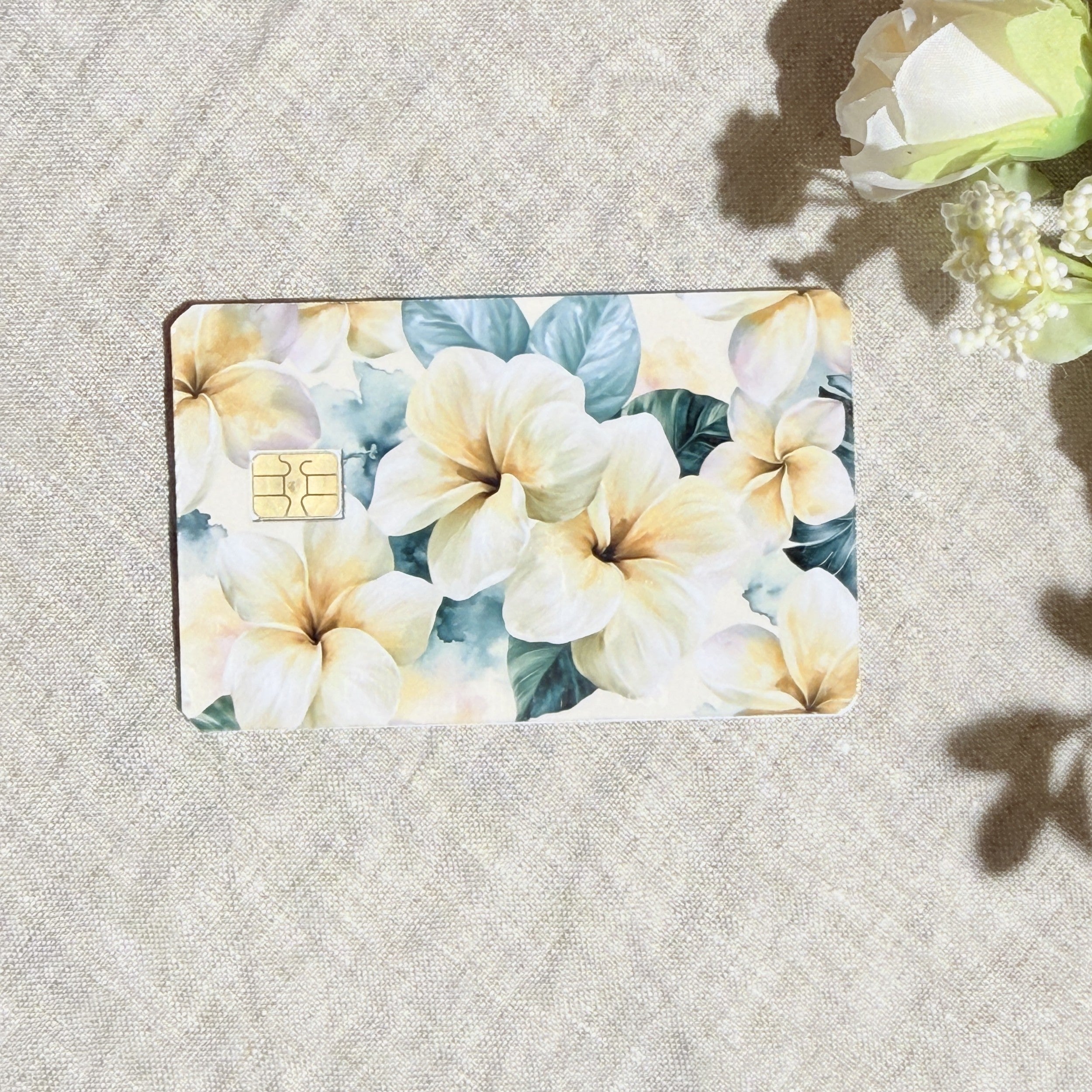 Plumeria card skin with cream and yellow tropical flowers on sage leaves on a debit card by The Sticker Era