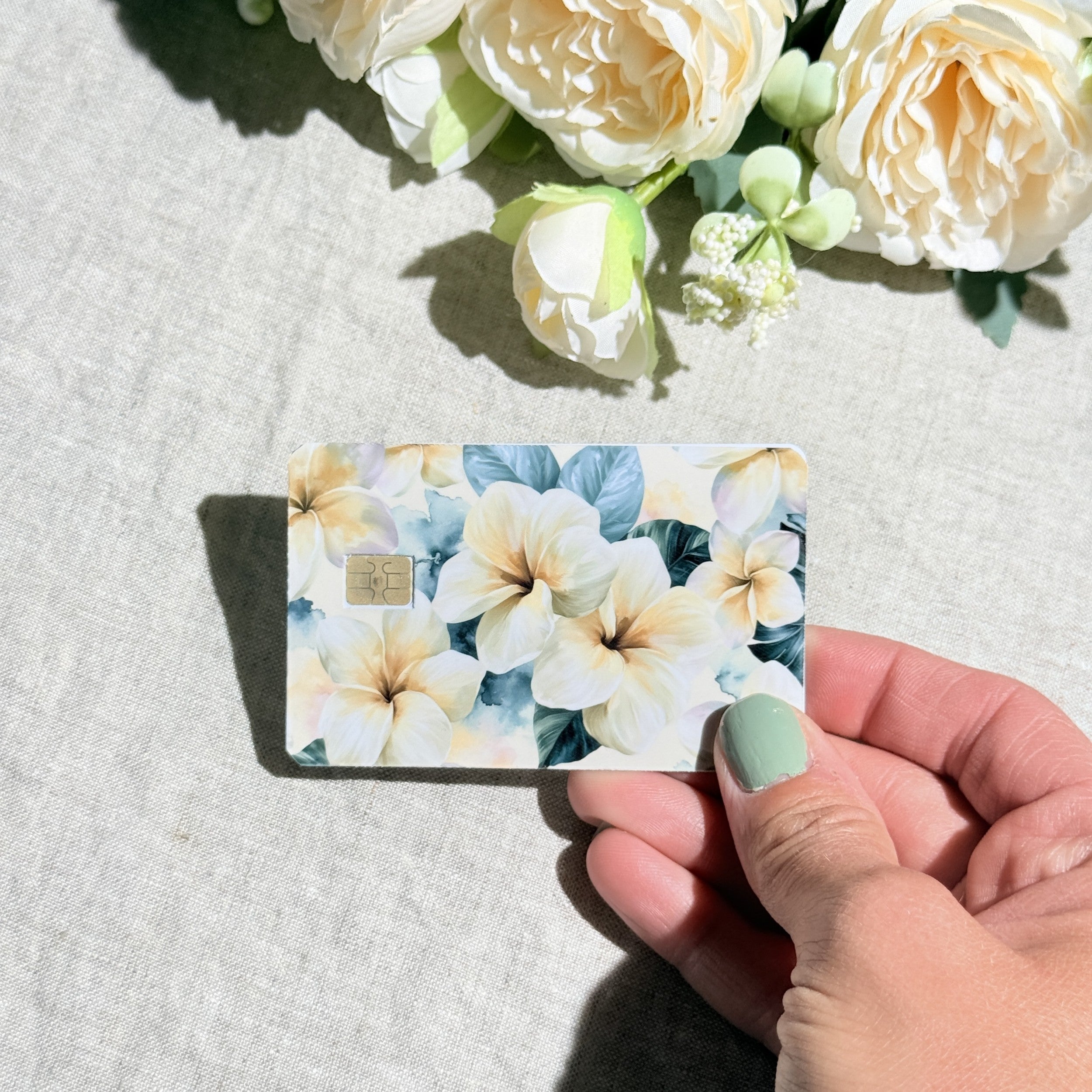 Hand holding the plumeria debit card skin in sunlight by The Sticker Era