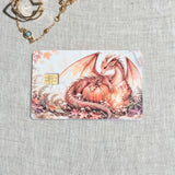 Pumpkin dragon card skin on a debit card, coral dragon curled around a pumpkin in autumn leaves