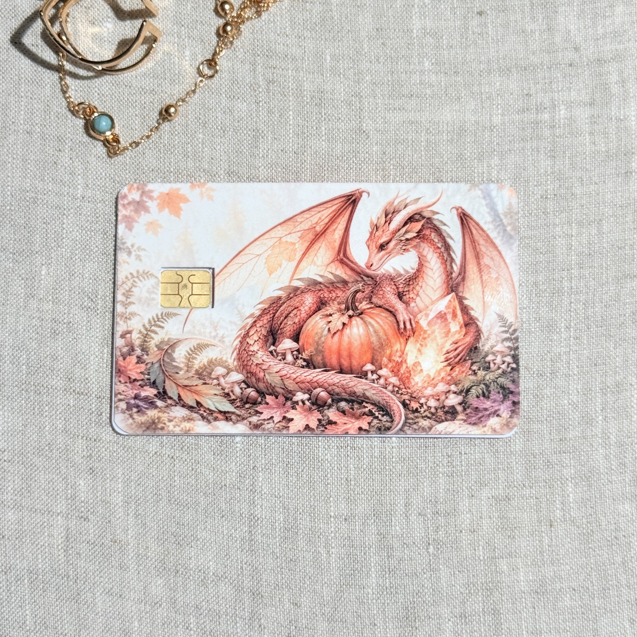 Pumpkin dragon card skin on a debit card, coral dragon curled around a pumpkin in autumn leaves