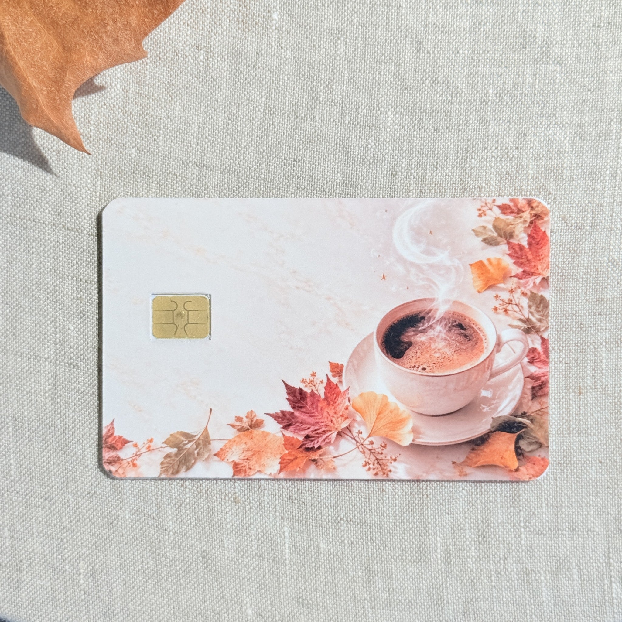 Pumpkin spice latte card skin on a debit card, pink coffee cup on cream marble with maple leaves
