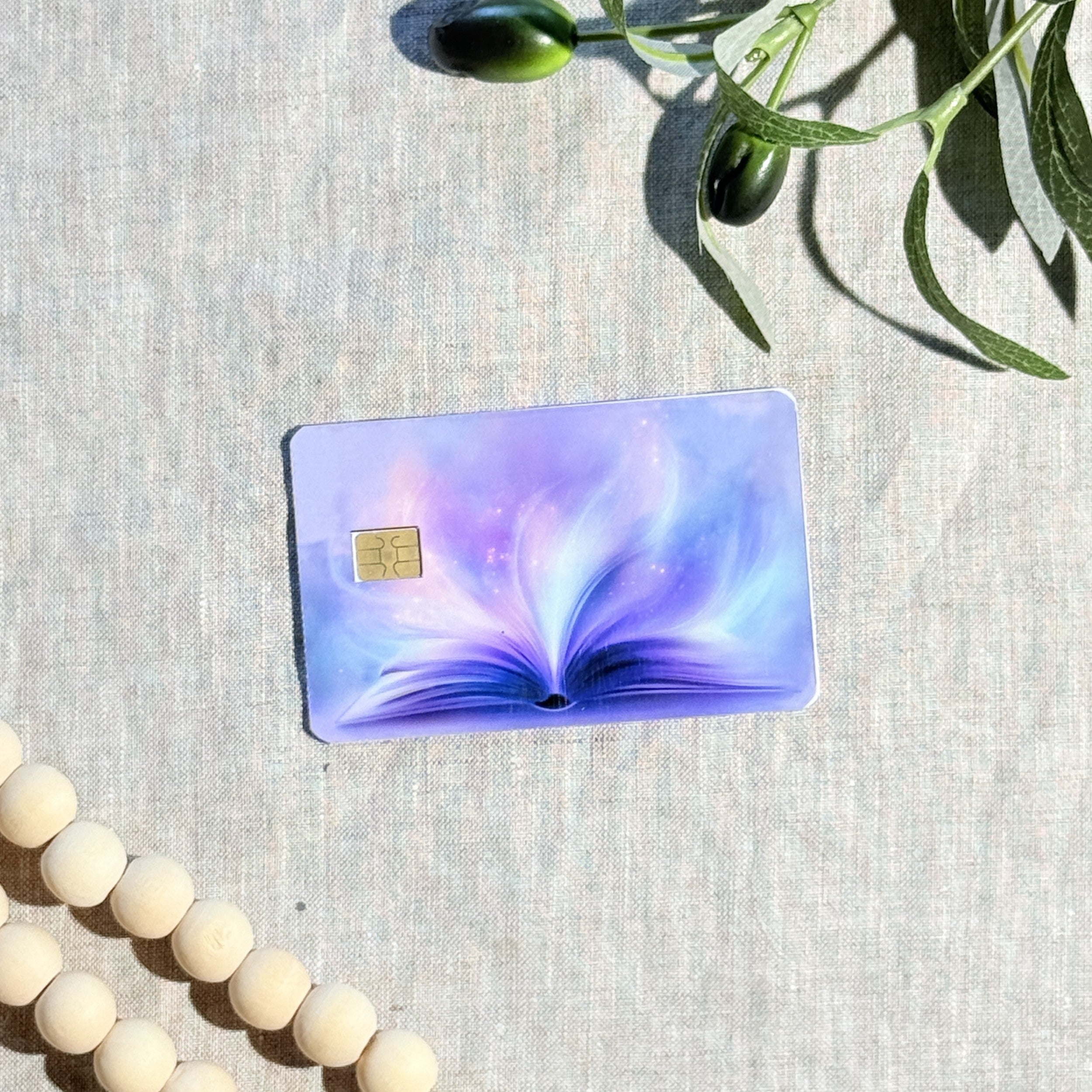 Purple magic book card skin with glowing open book on a lavender debit card by The Sticker Era