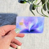 Purple glowing open book debit card skin flat lay on linen by The Sticker Era
