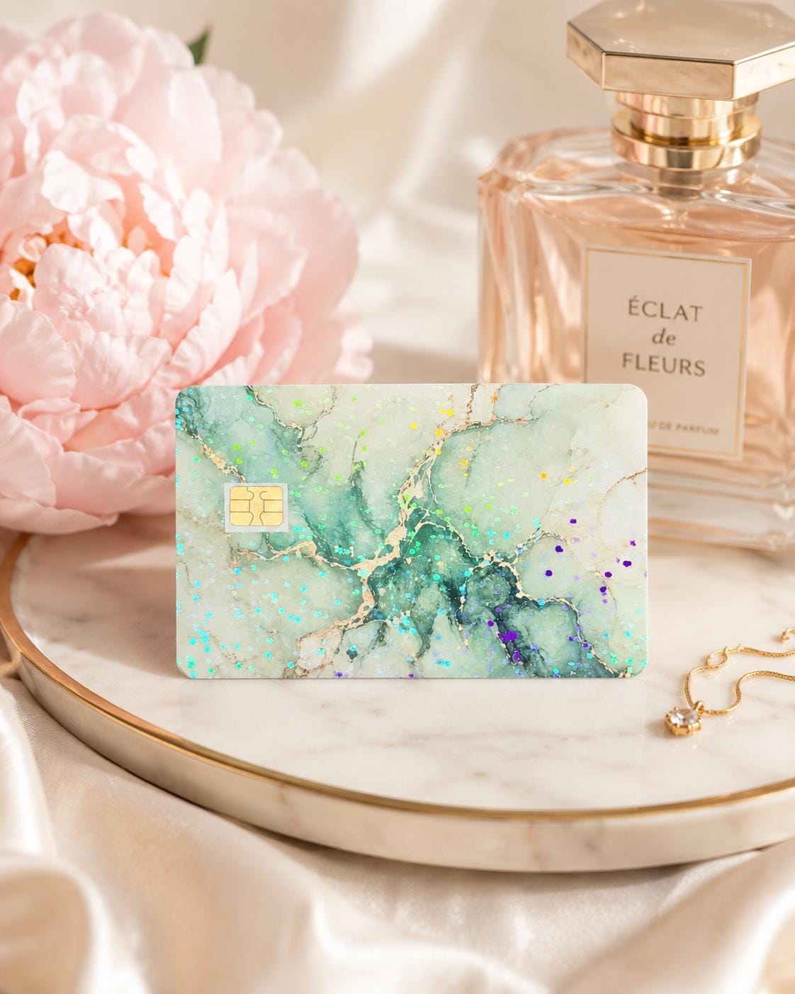 Sage green marble debit card skin on a marble tray beside a peony and perfume by The Sticker Era