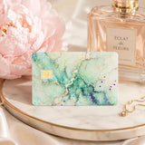 Sage green marble debit card skin on a marble tray beside a peony and perfume by The Sticker Era
