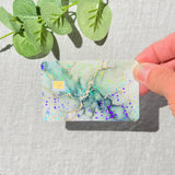 Hand holding the sage green marble card skin in sunlight showing the holographic sparkle by The Sticker Era