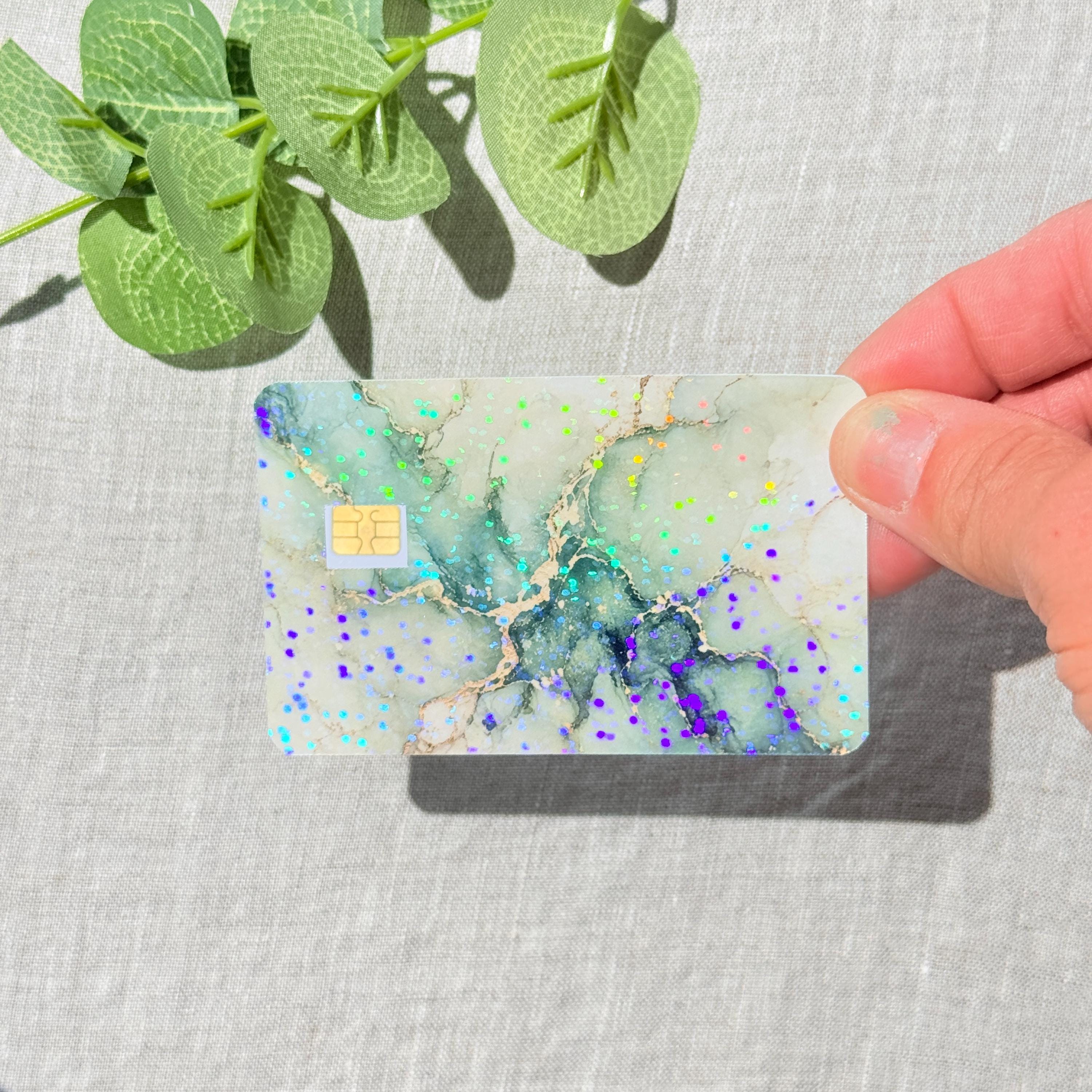 Hand holding the sage green marble card skin in sunlight showing the holographic sparkle by The Sticker Era