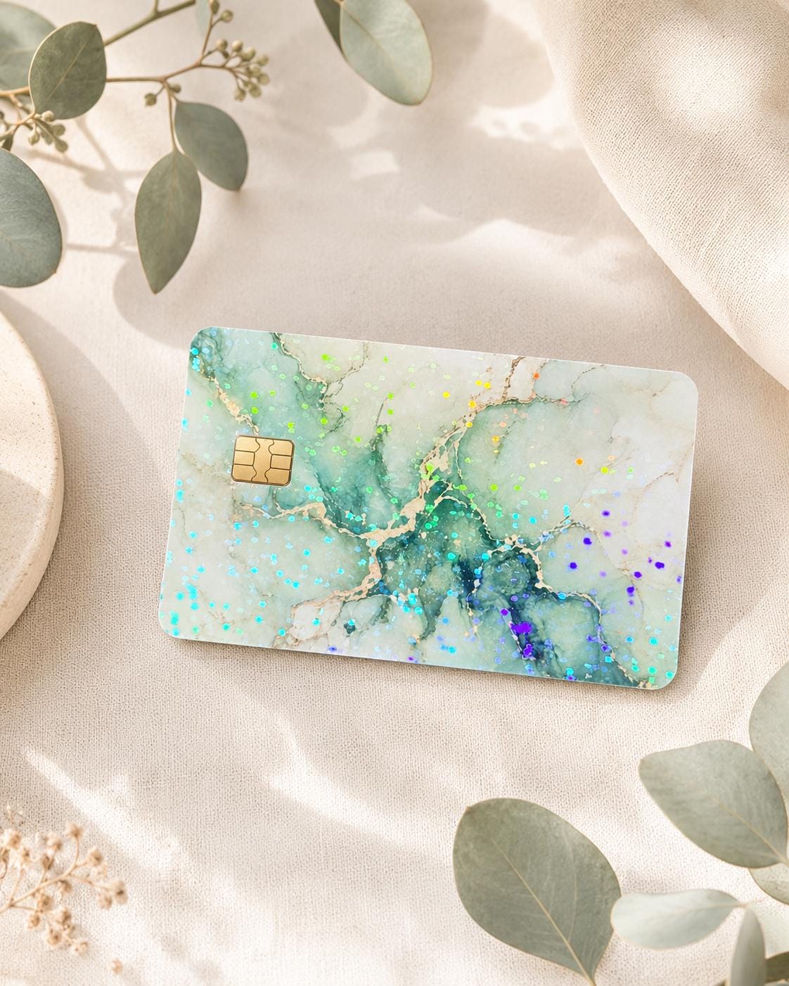 Green marble debit card skin on cream linen with eucalyptus leaves by The Sticker Era