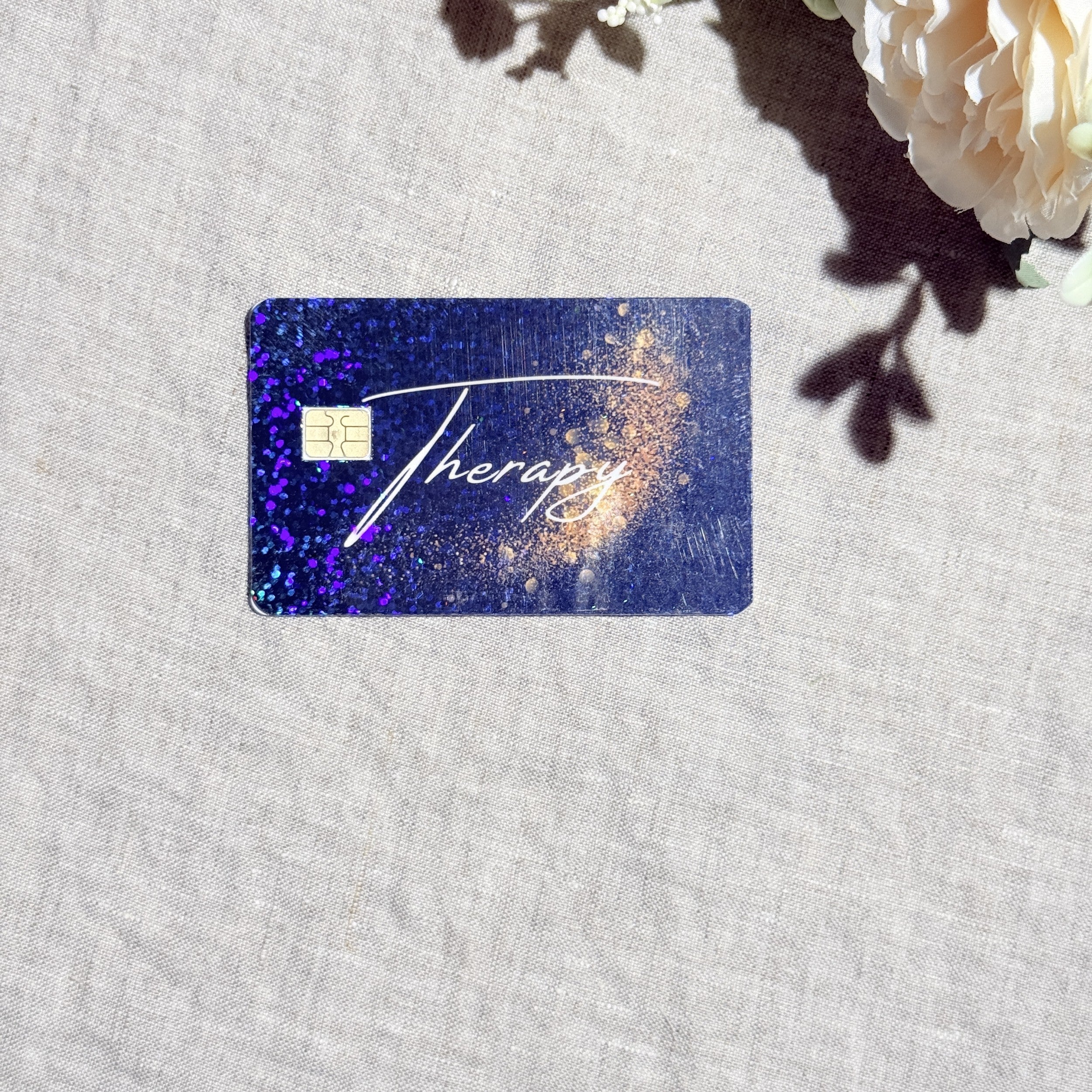 Therapy card skin with gold script and holographic sparkle on a navy galaxy debit card by The Sticker Era